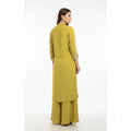 Mannequin wearing a yellow outfit with intricate detailing in a room setting.
